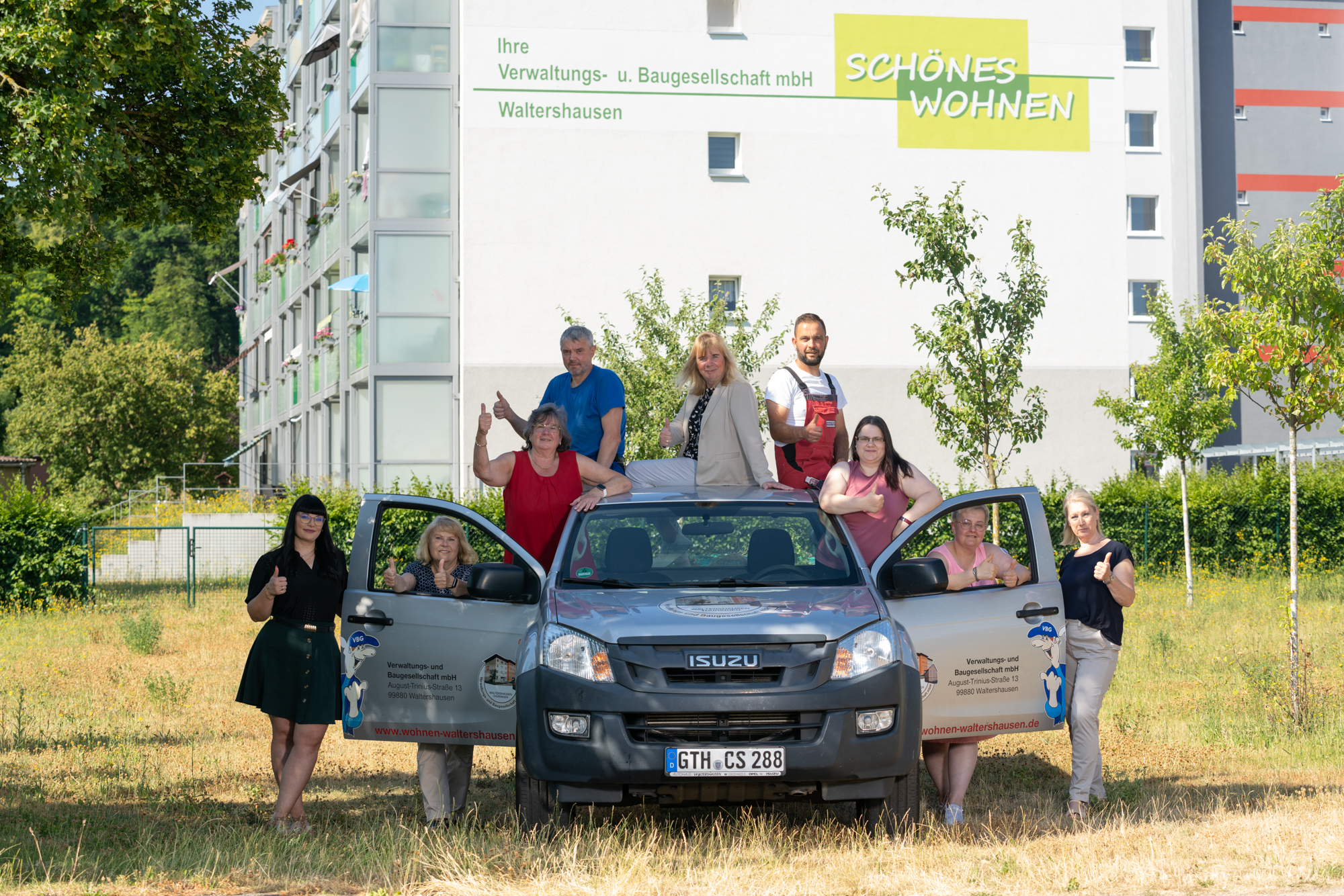 Das gesamte Team der Verwaltungs- und Baugesellschaft mbH um einen Isuzu drumherum platziert, steht vor dem Mietobjekt in Ibenhain. Alle strahlen Kompetenz, Ruhe und Professionalität aus.